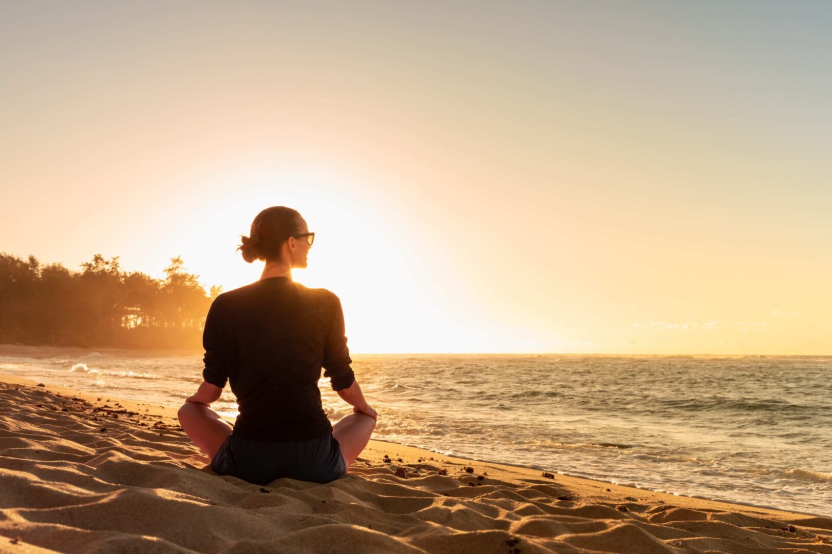 Woman sitting on beach at sunset.