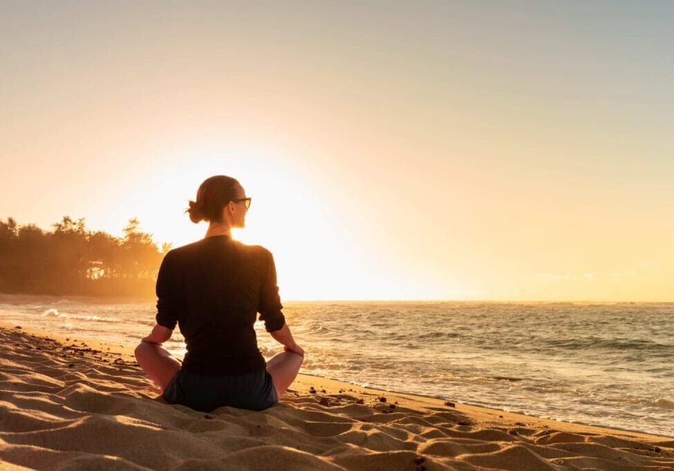 Woman sitting on beach at sunset.